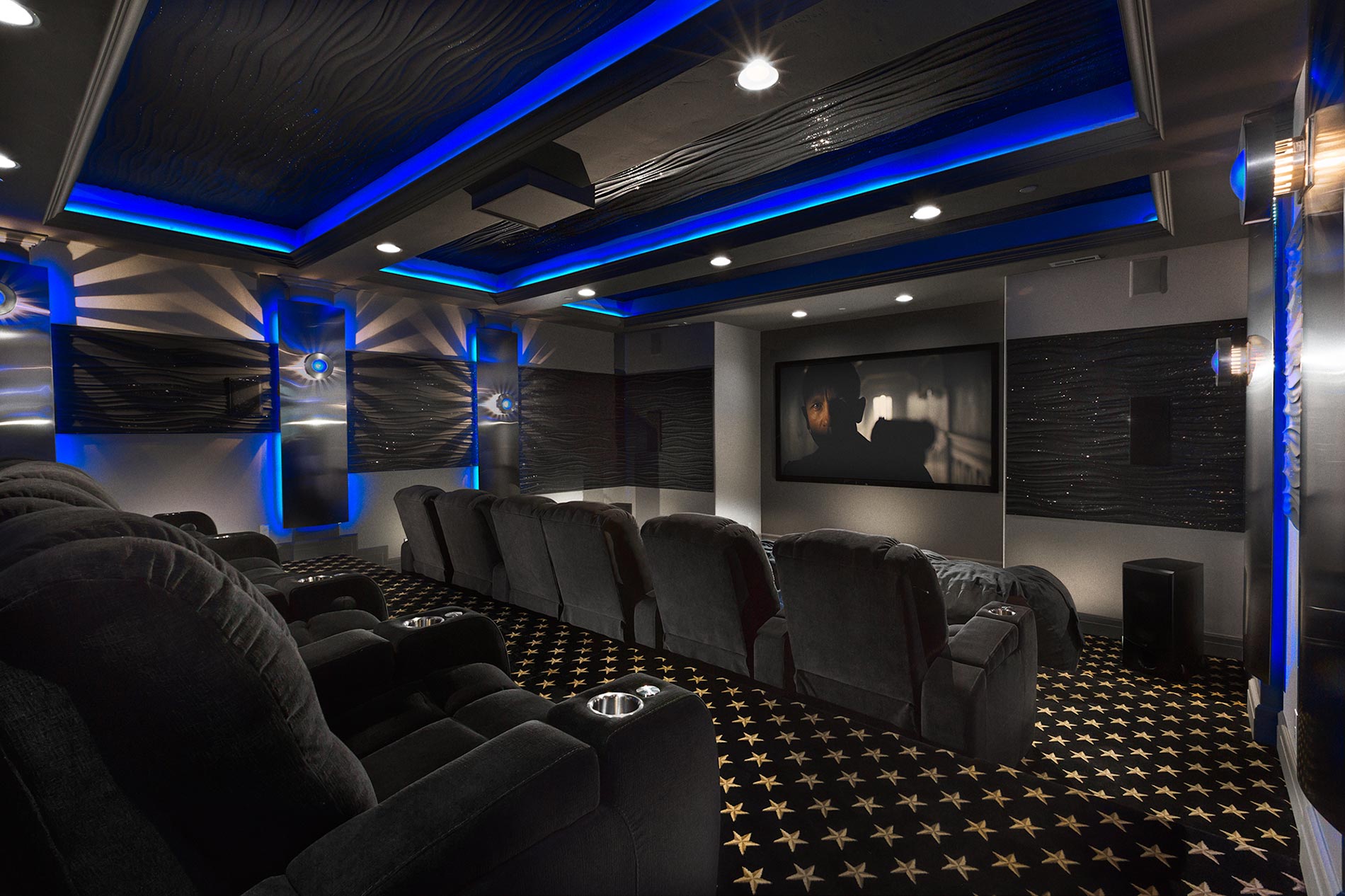 A luxurious home theater featuring comfortable reclining seats, a large screen, and vibrant blue accent lighting.