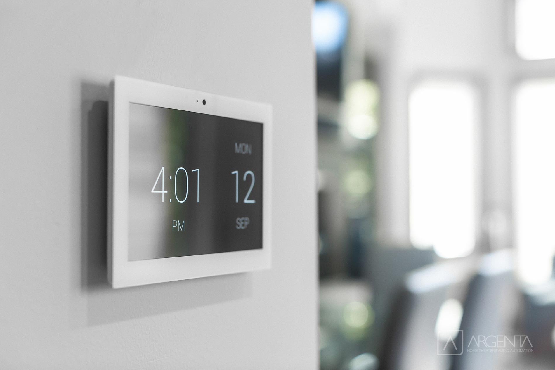 A smart wall panel displaying time and date in a bright, modern living space.